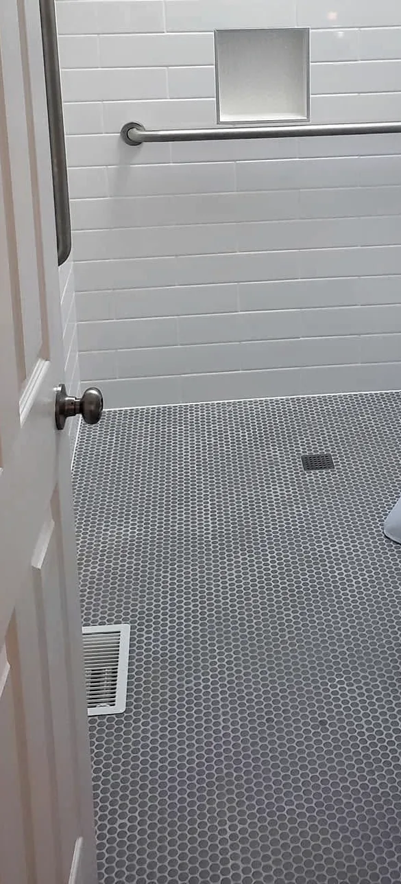 The same shower seen from the bathroom door: the grey penny tile runs from the room into the shower with no curb or step.