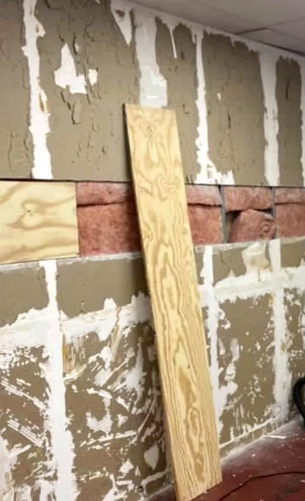 A kitchen wall with the old panels stripped off, leaving patches of brown backing and white glue.
