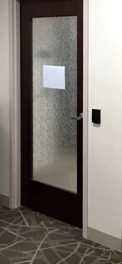 The reception door Patton moved forward: a door with a frosted glass panel, its handle and a card reader on the white wall.