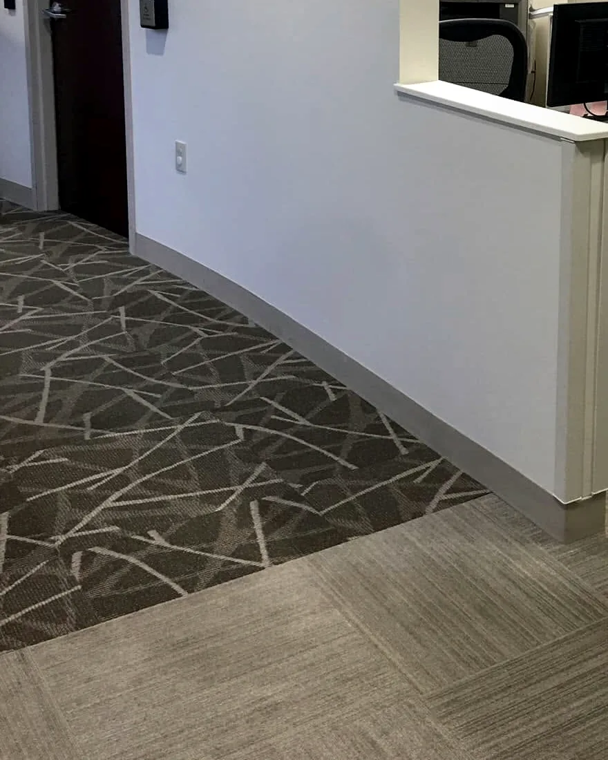 The office reception after the work: a new curved half-height wall with a white cap beside the check-in counter, and a door with a card reader behind it.