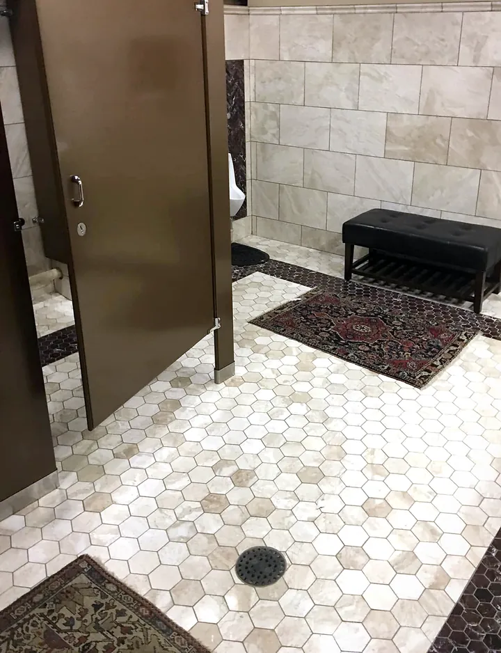 The same restroom, wider: the hex mosaic and its dark border run past the stall doors to the bench under the wall tile.